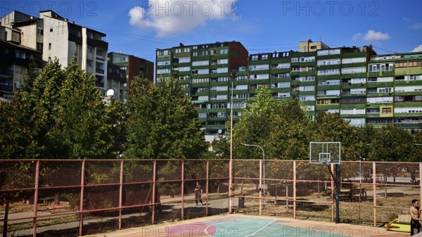 A basketball court surrounded by apartment blocks and trees, in sunny weather, Pristina, Kosovo