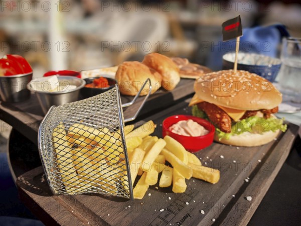 Burger with fries served on a wooden tray, with cheddar cheese, lettuce and tomatoes, in a sunny atmosphere, Prizren, Kosovo