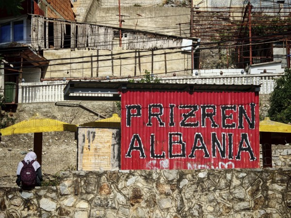 Red sign with the inscription Prizren Albania in front of building and road, Prizren, Kosovo