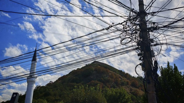 Several power lines in front of a minaret and a wooded hill, Prizren, Kosovo