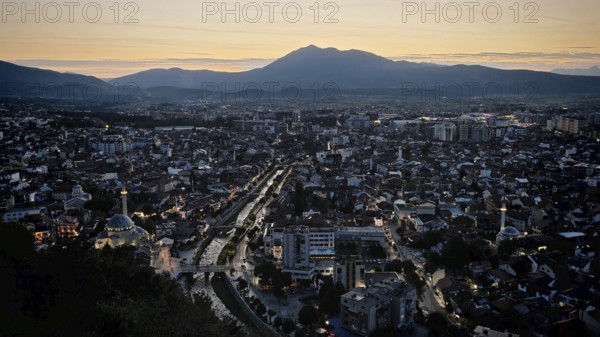Night view of city with glowing lights, river and mountain skyline in the background, Prizren, Kosovo