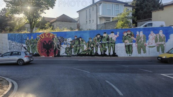 Wall painting of soldiers with KLA emblem on a street corner, Kosovo