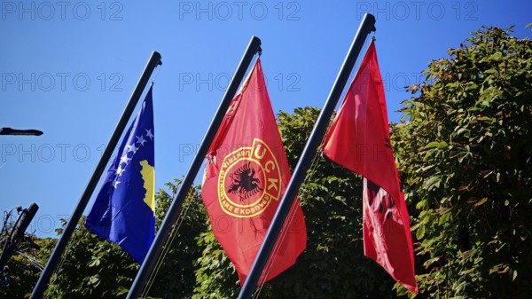 Three flags of Kosovo, USK, Albania fly against green background and blue sky, Kosovo