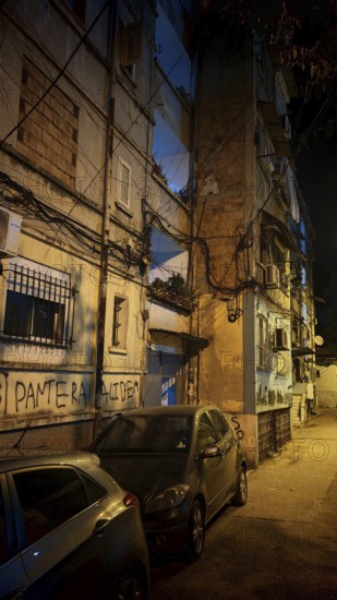 Night view of a city street with parked cars and worn buildings, Tirana, Albania