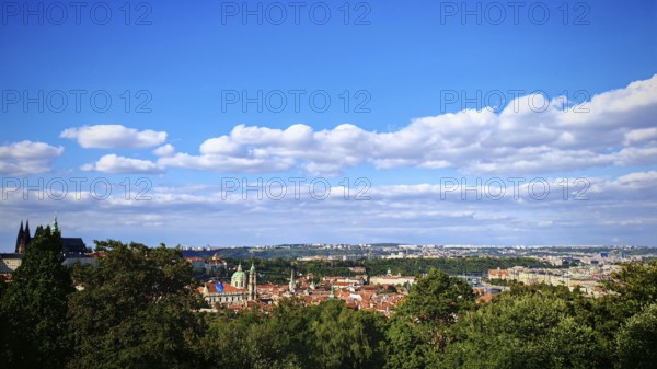 City panorama with distinctive buildings and green hills under a blue sky, view over Prague, Czech Republic