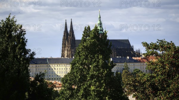 Gothic church between tall trees, cloudy sky in the background, view of Hradcany, Prague, Czech Republic