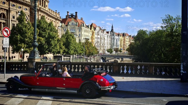Driving a classic car, sightseeing, sightseeing along a street lined with historic buildings in sunshine, Prague, Czech Republic