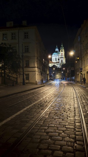 Illuminated cobblestone street with tram tracks at night with a view of a cathedral, Prague, Czech Republic
