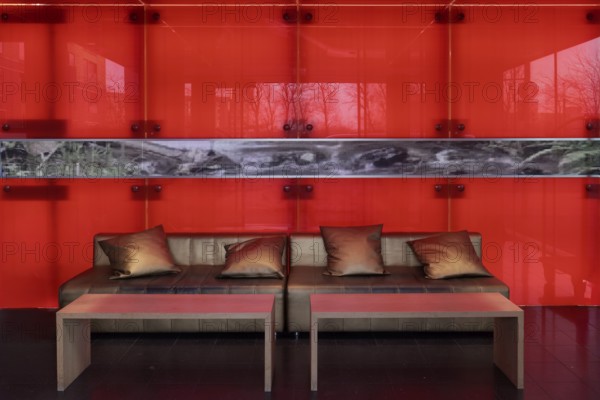Sofa with golden cushions in front of a red-illuminated glass wall, stylish lobby of an apartment building, Düsseldorf, North Rhine-Westphalia, Germany