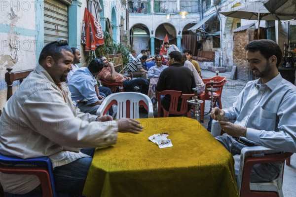 Tripoli, Libya, North Africa. Man playing cards and others smoking shisha in a traditional 'funduq' in the centre of Tripoli