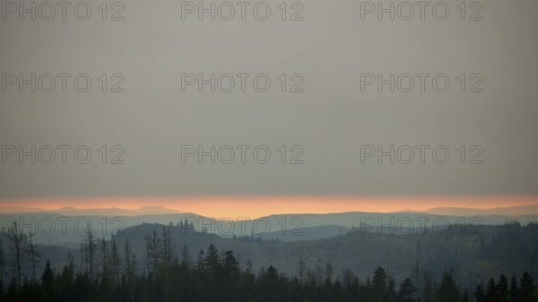 Forest and mountains at dusk below a cloudy horizon, with Staffelberg on a glowing horizon, Frankenwald nature park Park