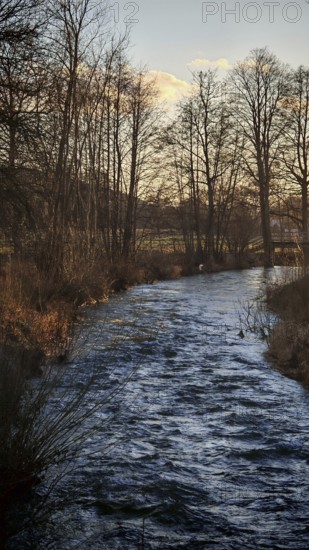 A quiet river flows through a winter landscape lined with bare trees, Franconian Forest nature park Park