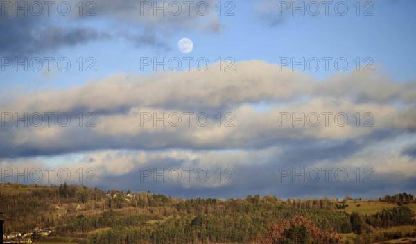 A peaceful landscape with forest and moon in a blue sky, surrounded by clouds, Franconian Forest nature park Park