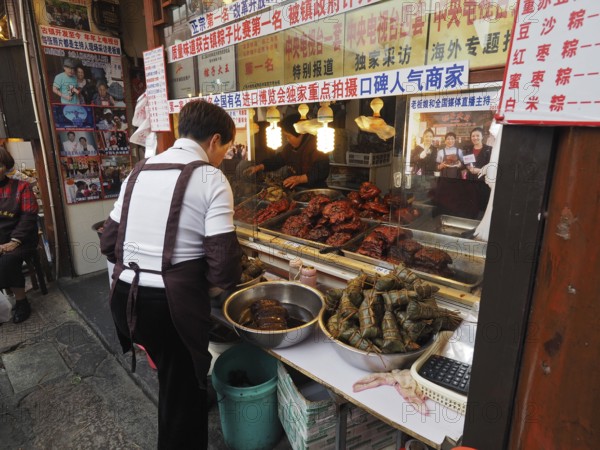 A saleswoman stands at a busy market stall with a variety of exotic foods, Zhujiajiao Ancient Town, Shanghai, China
