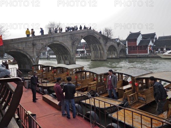 People on a stone bridge admire the wooden boats on the river in a historic city setting, Zhujiajiao Ancient Town, Shanghai, China