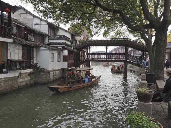 Traditional bridge over a canal with boats flanked by old houses and trees, Zhujiajiao Ancient Town, Shanghai, China