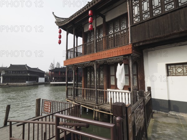 A traditional wooden house with red lanterns on the riverbank in a peaceful setting, Zhujiajiao Ancient Town, Shanghai, China