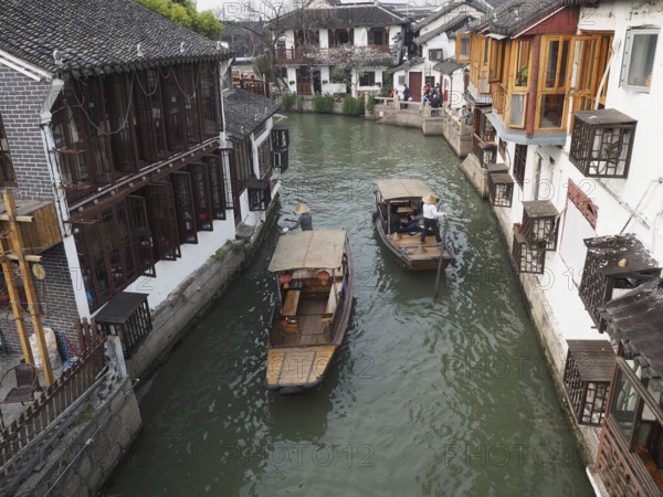 Two boats sail through a narrow canal lined with traditional Chinese buildings, Zhujiajiao Ancient Town, Shanghai, China