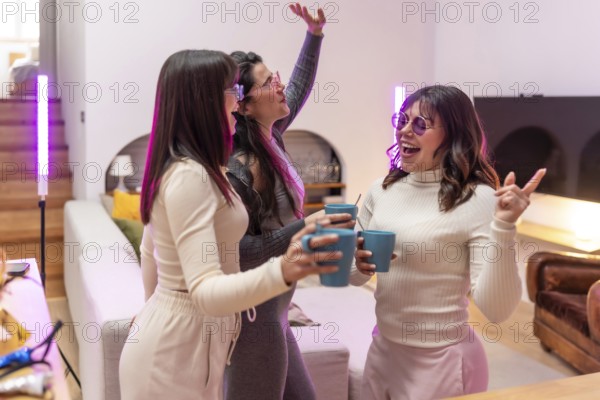 Three young women laughing and celebrating with drinks in a cozy apartment living room, purple pink party lighting creating a vibrant, candid moment of friendship and joy