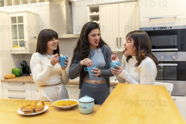Three young women laughing and chatting around a kitchen island, sharing muffins and hot drinks in a cozy morning scene that captures friendship, casual bonding, and home life