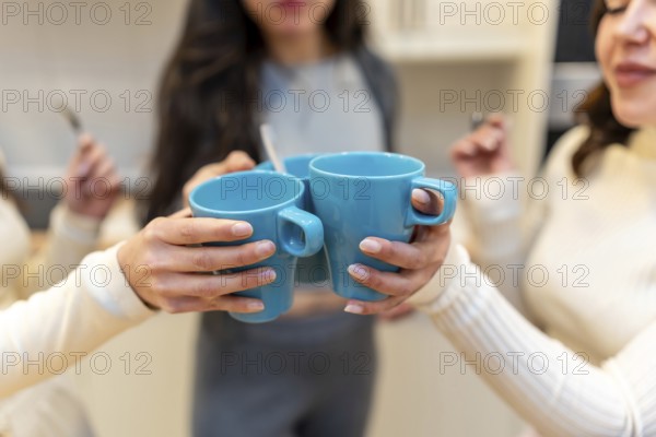 Close up of friends clinking bright blue mugs together in a warm kitchen, celebrating friendship and good vibes during a cheerful morning coffee moment