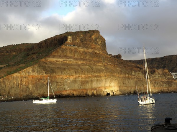 Rocks on calm sea with boats and golden evening sun, Puerto de Mogan, Gran Canaria, Canary Islands, Canary Islands, Spain