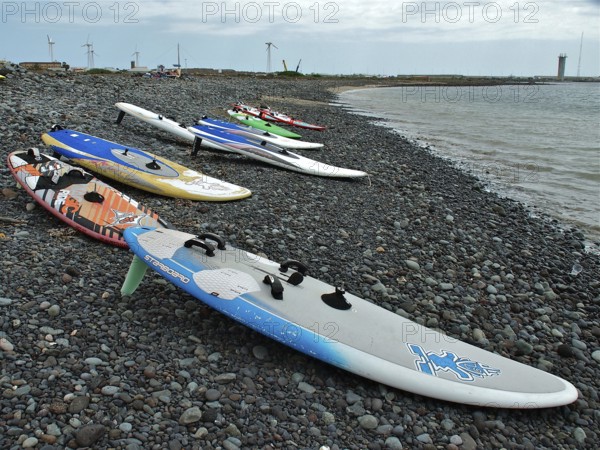 Pebble beach with colorful surfboards at sea under cloudy sky, Pozo Izquierdo, Gran Canaria, Canary Islands, Canary Islands, Spain