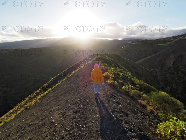 Female hiker walks along a sunlit hill with extensive shadows, Caldera de Bandama volcanic crater, Gran Canaria, Canary Islands, Spain