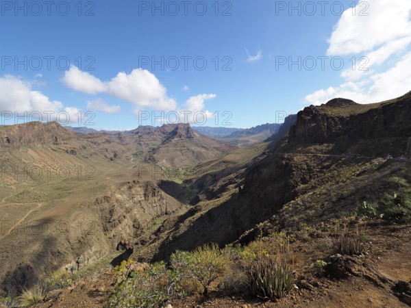 Arid mountain landscape with rocks and wide valley under a blue sky with clouds, Barranco de Fataga, Gran Canaria, Canary Islands, Spain