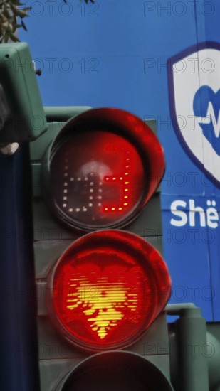 Traffic light shows red light with Tiran flag eagle against blue background in an urban environment, Tirana, Albania