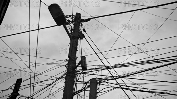 Black and white shot of numerous wires twisting around a power pole against a cloudy sky, Tirana, Albania
