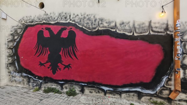Graffiti depicting the flag of Albania with a black eagle on a red background on a wall along a path, Tirana, Albania