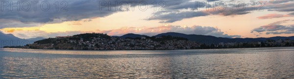 Evening panorama of a lake with mountains and a city in the background under dramatic sky, Lake Ohrid, North Macedonia
