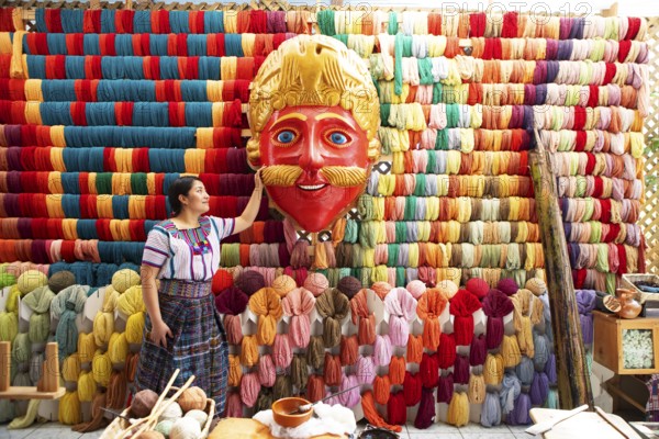 Maya woman, 42 years old, looks at the mask of a Moro or Moor for the traditional mask dance, behind it a wall full of colorful cotton, traditional crafts in a woman's cooperative, San Juan la Laguna, Atitlán, Sololá Department, Guatemala