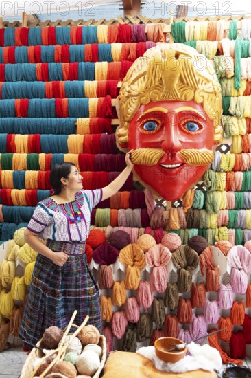 Maya woman, 42 years old, looks at the mask of a Moro or Moor for the traditional mask dance, behind it a wall full of colorful cotton, traditional crafts in a woman's cooperative, San Juan la Laguna, Atitlán, Sololá Department, Guatemala
