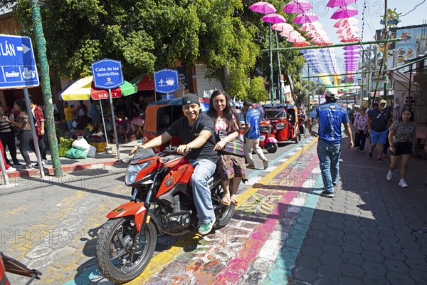 Mayans wearing traditional and modern clothes on a motorcycle in an alley in San Juan la Laguna, Atitlán, Sololá Department, Guatemala