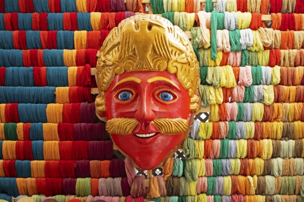 Mask of a Moro or Moor for traditional mask dance, behind a wall full of colorful cotton, traditional crafts in a woman's cooperative, San Juan la Laguna, Atitlán, Sololá Department, Guatemala