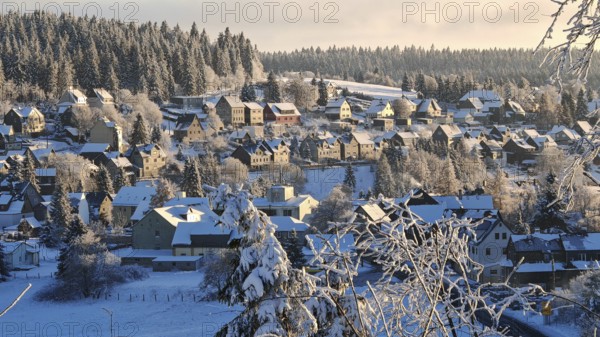 Snowy village in front of wooded hills under blue skies, Rennsteig, Thuringian Forest nature park Park