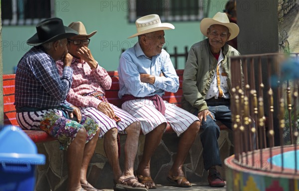 Guatemalan men wearing Coxboy hats sitting laughing on a bench in Santiago de Atitlán, Sololá Department, Guatemala