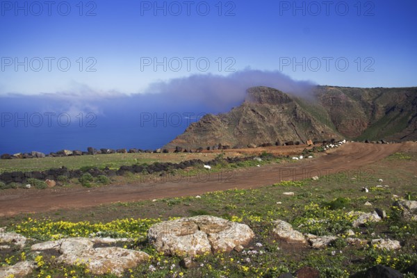 A narrow path high up in the mountains of the Famara massif with views of the sea with clouds in the blue sky, Mirador de Ermita de Las Nieves, Lanzarote