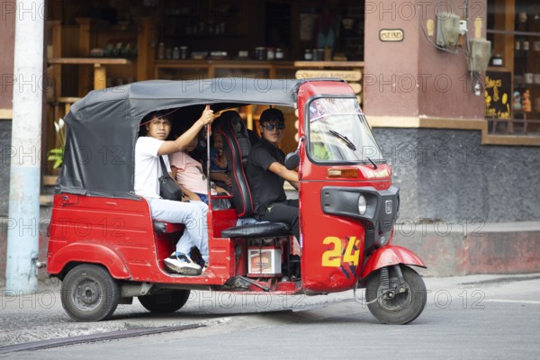 Red tuk tuk or tricycle taxi with Guatemalan passengers in Panajachel, Atitlán, Sololá Department, Guatemala
