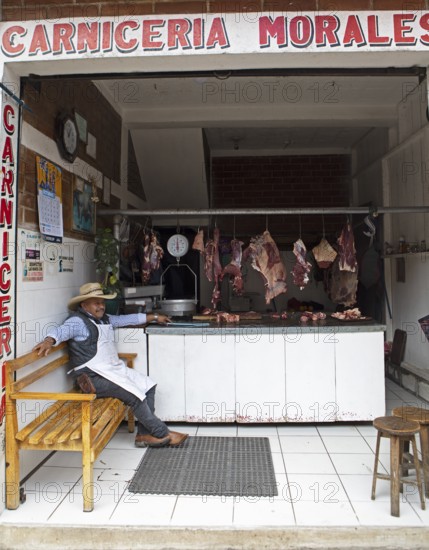 Guatemalan man wearing cowboy hat sits in a butcher shop in Chichicastenango, Highlands, El Quiché Department, Guatemala