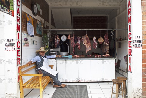 Guatemalan man wearing cowboy hat sits in a butcher shop in Chichicastenango, Highlands, El Quiché Department, Guatemala