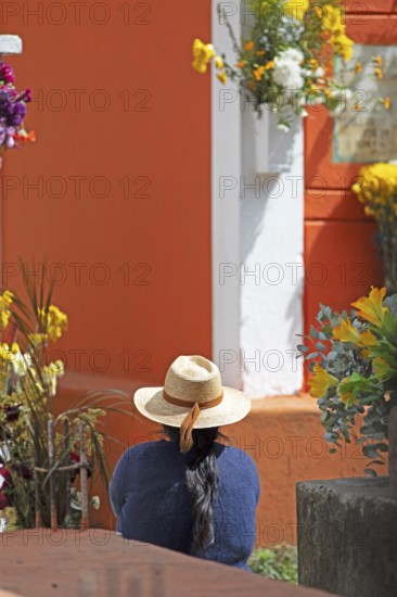 Mayan woman wearing straw hat looking at a colorful grave in the cemetery in Chichicastenango, Highlands, El Quiché Department, Guatemala