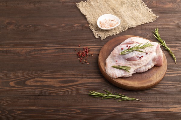 Raw Turkey Thigh with spices and rosemary on cutting board on brown wooden background and linen textile. side view, copy space