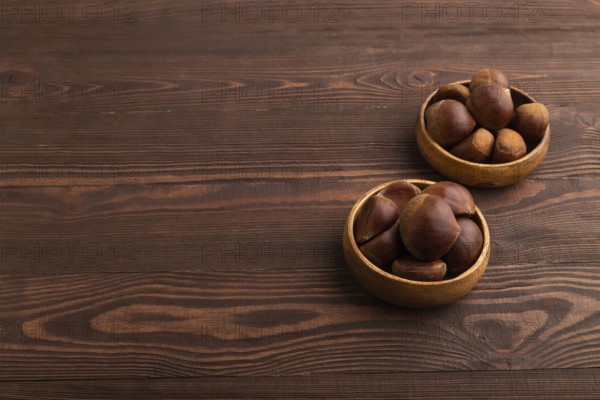 Wooden bowl with raw edible ?hestnuts on brown wooden background, side view, copy space, minimalism