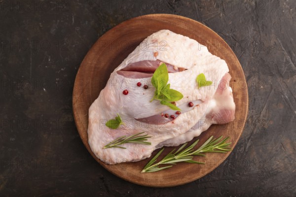 Raw Turkey Thigh with spices and rosemary on cutting board on black concrete background. top view, flat lay, close up