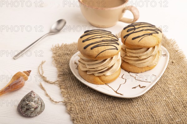 Caramel Cream Cakes on white wooden background and linen textile, cup of coffee, side view, close up
