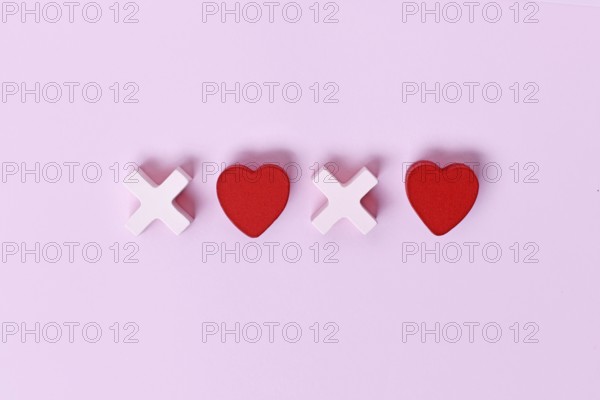 Valentine flat lay with wooden light pink and red hearts forming XOXO letters arranged on a pink background. Love, hugs and kisses holiday message