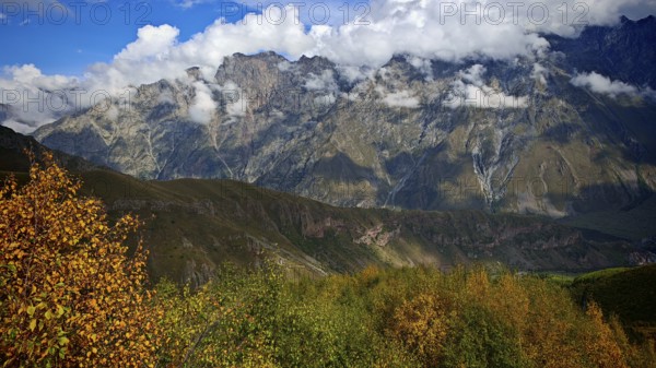 A mountainous landscape with dramatic clouds and golden autumn trees, Stepantsminda, Georgia